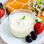 Japanese custard pudding in a glass cup served with fresh strawberries and blackberries topped with whipped cream and mint leaves, side angle shot.