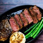Japanese style garlic steak cut into slices served on a cast iron plate with garlic and green beans, top down shot.