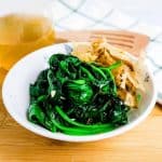 Lightly salted garlic spinach stir fry served in a side dish bowl topped with Japanese katsuoboshi, side angle.