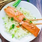 Japanese marinated miso salmon served over a bed of rice topped with chopped green onions being picked up with a pair of chopsticks.