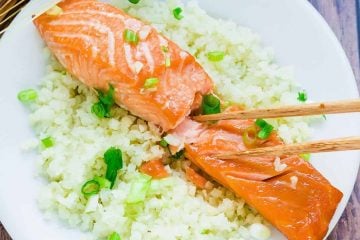 Japanese marinated miso salmon served over a bed of rice topped with chopped green onions being picked up with a pair of chopsticks.