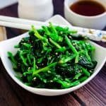 Korean style spinach salad seasoning with salt and garlic served cold in a white bowl with a pair of chopsticks.
