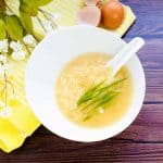 Chinese style egg drop soup served in a white bowl topped with green onions, top down shot.