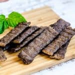 Spicy teriyaki style beef jerky sticks served in a cup and on a wooden plank.