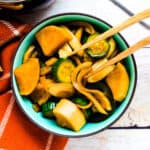Pickled Korean vegetables in a side dish bowl being picked up with a pair of chopsticks.