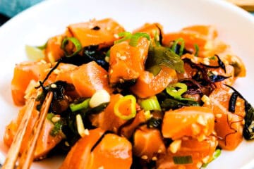 Homemade salmon poke recipe served in a bowl topped with seaweed and fresh chopped green onions, close up shot.