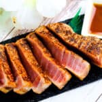 Seared blackened ahi tuna steak served on a black slate with soy sauce mixed with wasabi.