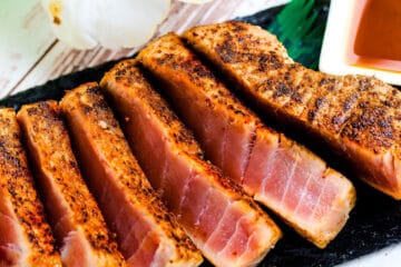 Seared blackened ahi tuna steak served on a black slate with soy sauce mixed with wasabi.