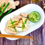Asian style steamed boneless Hainan chicken top with green onions served on a plate with ginger salt dipping sauce, top down shot.