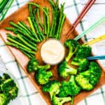 Boiled asparagus and broccoli served on a wooden plate with a bowl of Japanese style miso mayo sauce, top down shot.