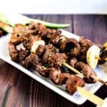 Beef kushiyaki served on a white plate sprinkled with toasted sesame seeds.