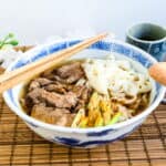 Beef udon served in a Japanese style noodle bowl with a pair of wooden chopsticks.