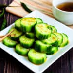 Din Tai Fung Cucumber Salad marinated in a chili oil marinade served on a white plate topped with toasted sesame seeds.