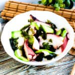 Tako su served in a white bowl mixed with seaweed and topped with toasted sesame seeds.