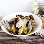Steamed Manila clams in a white wine broth topped with chopped green onions served in a white bowl with a sliver fork.
