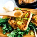 Pan fried Asian style garlic pork chops topped with green onions served on a wooden plank with garlic soy sauce being poured over.