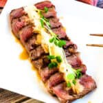 Japanese style beef steak tataki served on a white plate topped with radish sports and grated daikon.