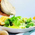 Caesar dressing being poured on top of romaine lettuce topped with fresh parmesan cheese.