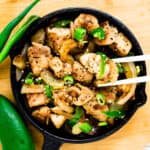 Chicken stir fry with sesame oil in a cast iron pan being picked up with a pair of chopsticks.