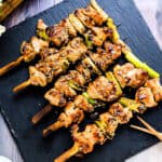 Japanese grilled chicken skewers yakitori negima served on a black plate garnished with toasted sesame seeds.
