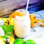 Peaches and cream smoothie served in a mason jar with a straw and peach slice on the rim.