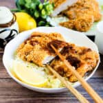 Japanese pork tonkatsu served over a bed of cabbage with a wedge of lemon and Japanese tonkatsu sauce.