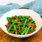 Sauteed bacon garlic green bean recipe served in a white bowl topped with toasted sesame seeds, close up shot.