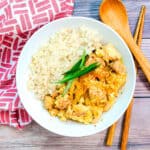 Chicken donburi oyakodon served in a white bowl topped with Japanese chili powder and chopped green onions.