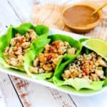 Chicken lettuce wraps served with Thai peanut dipping sauce and a slice of lime.