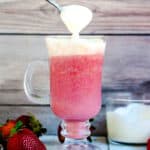 Cream cheese foam being whipped with a spoon into strawberry smoothie.
