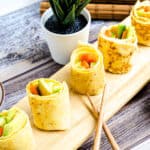 Egg roll sushi with vegetables served on a wooden board with a pair of chopsticks and soy sauce.