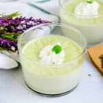 Matcha panna cotta served in a glass cup topped with whipping cream and a mint leave.