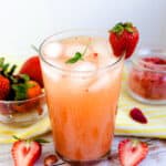 Strawberry iced green tea served in a glass tumbler with fresh strawberry on rim of glass.