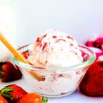 Strawberry milk ice cream served in a glass bowl being scooped up with a wooden spoon.