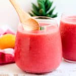 Strawberry slushie served in a cup and being scooped out with a wooden spoon.
