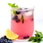 Blueberry mojito served in a glass tumbler topped with fresh blueberries.