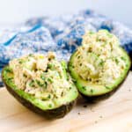 Stuffed avocado crab bowls topped with fresh parsley served on a wooden board.
