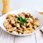 Garlic chicken stir fry garnished with chopped scallion green onions served in a white bowl.