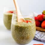 Matcha chia pudding served in a glass cup topped with fresh chopped strawberries being scooped up with a wooden spoon.