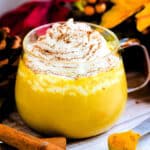 Turmeric Pumpkin Spice Latte served in a glass topped with whipping cream.