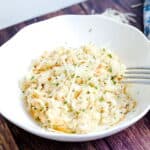 Cheese risotto made with cauliflower rice in a white dish topped with freshly chopped parsley served with a silver fork.