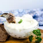 Slice of beef being dipped into garlic dip with a fork.