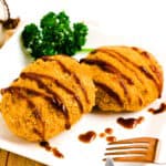 Japanese menchi katsu hamburger cutlet served on a plate with tonkatsu sauce drizzled over.