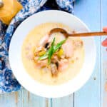Salmon bacon chowder served in a soup bowl with a golden spoon.