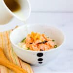 Salmon ochazuke broth being poured over rice topped with bonito flakes and baked salmon.
