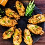 Japanese style fried garlic tebasaki chicken wings served on a black plate topped with green onions and garlic chips.