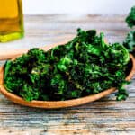 Crispy baked garlic kale chips served on a wooded plate.