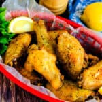 Fried lemon pepper wings served in a red basket with a wedge of lemon, side angle.