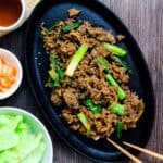 Korean BBQ bulgogi made with sliced ribeye served on a cast iron plate with green onions and toasted sesame seeds sprinkled on top.