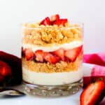 Strawberry parfait layered with a cheesecake crust served in a glass cup topped with sweetened strawberries.